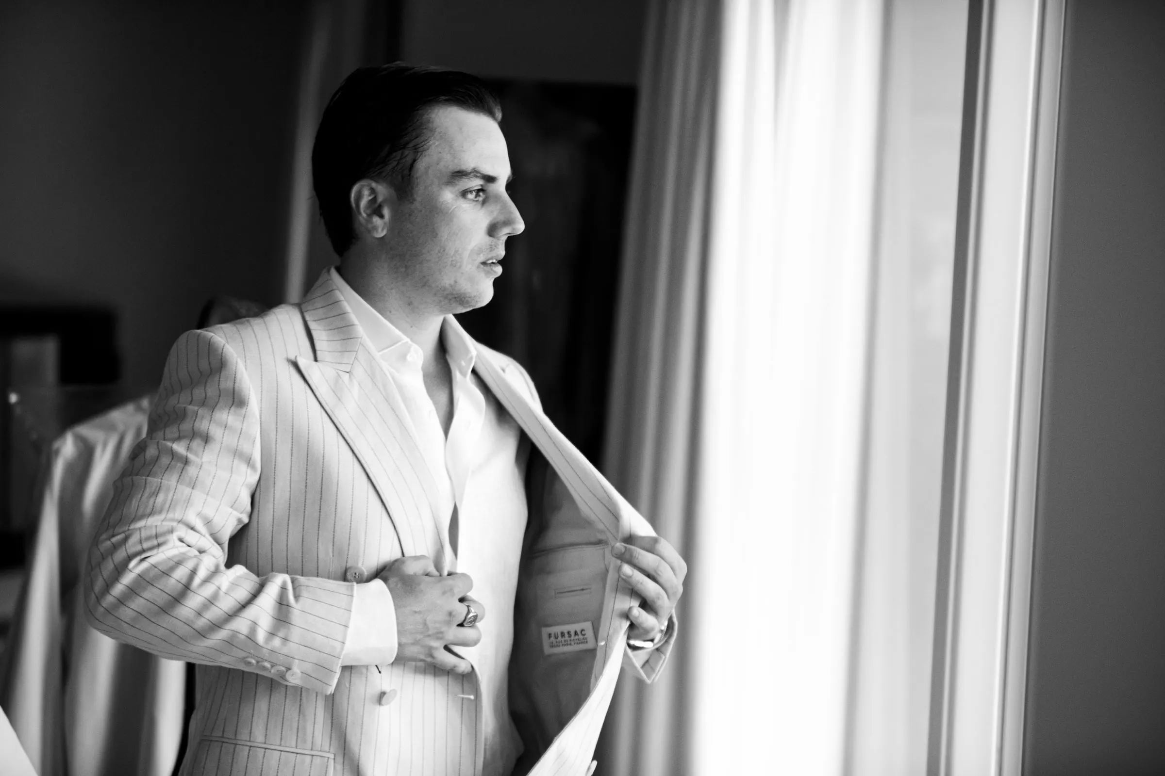 El novio se pone la americana de rayas junto a la ventana, en blanco y negro, Marbella