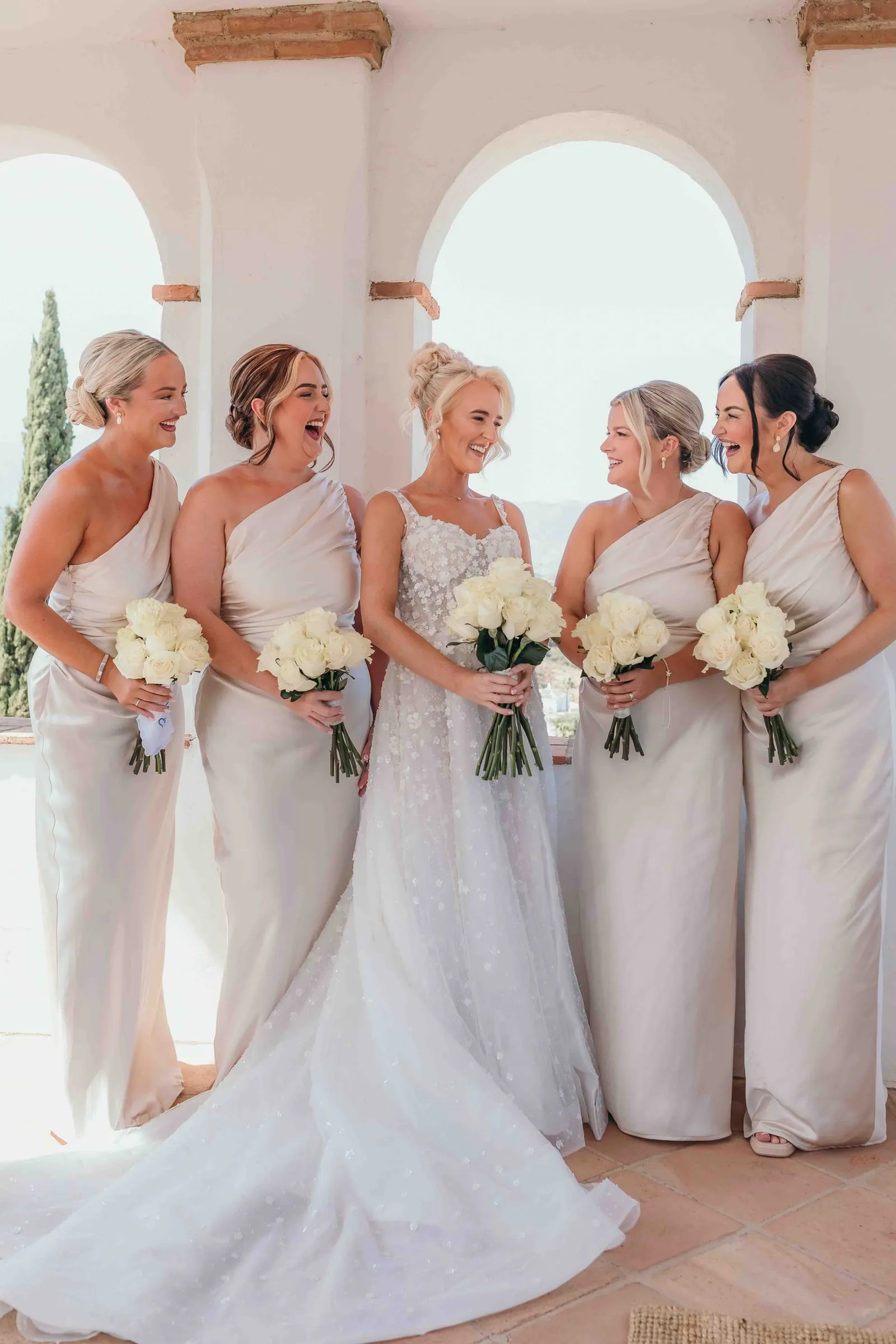 Bride and bridesmaids in white under the arches of a traditional hacienda