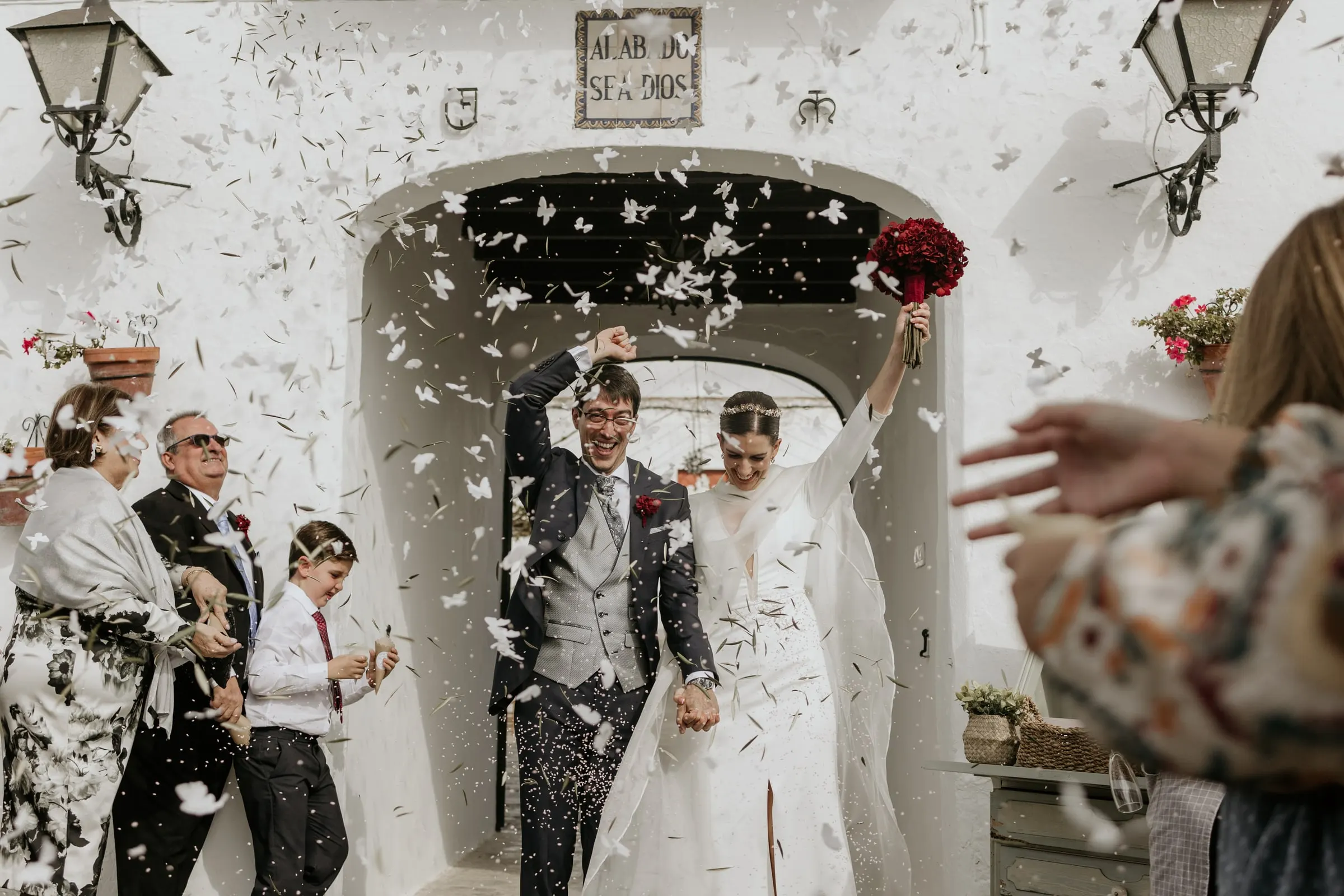Los recién casados salen por el arco del cortijo bajo una lluvia de pétalos de papel y un azulejo de «Alabado sea Dios»