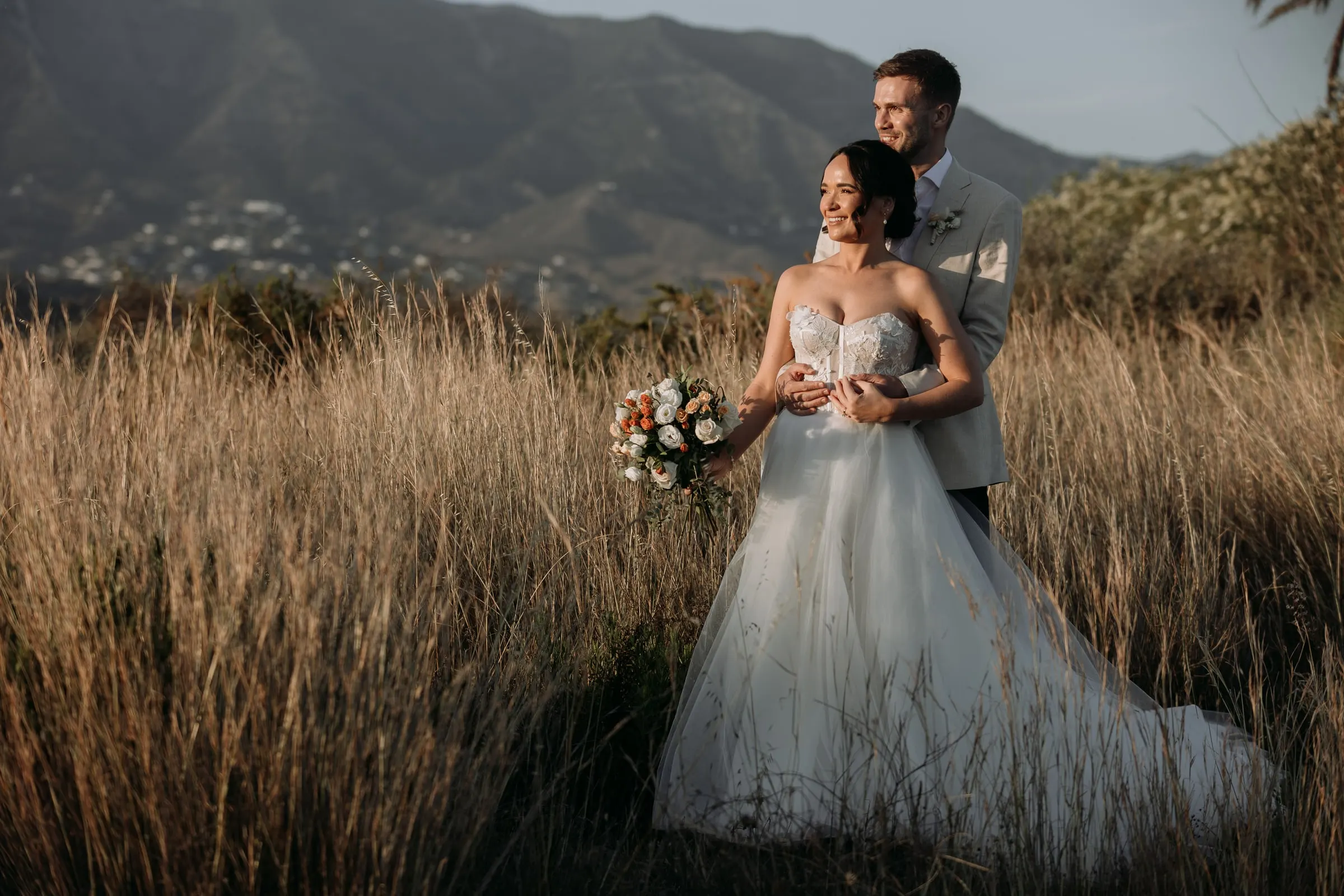 Los novios entre la hierba dorada al atardecer con la sierra de Mijas detrás