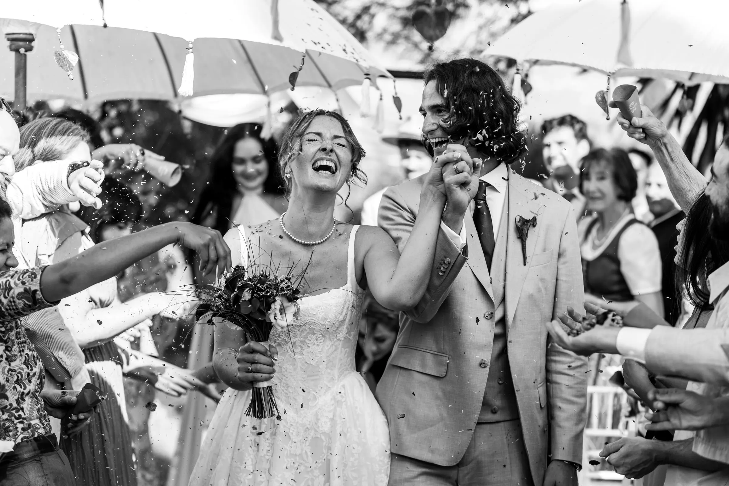 Los recién casados se ríen mientras los invitados les lanzan confeti, en blanco y negro, Hacienda San José, Mijas